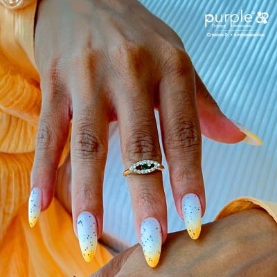 Mão com unhas pintadas degradê branco para amarelo e anel dourado com pedras verdes e brancas