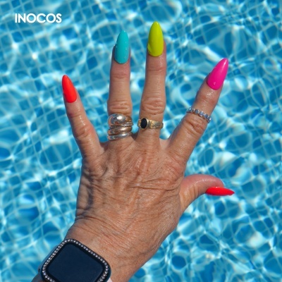 Mão com unhas coloridas e anéis sobre água de piscina azul