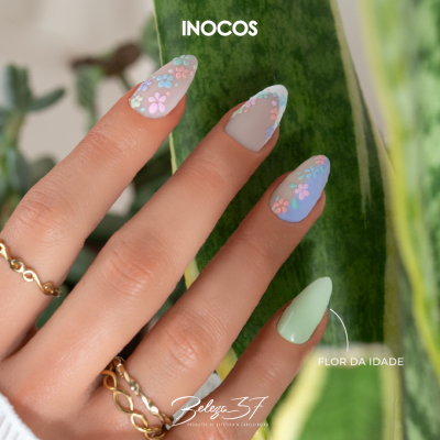 Unhas decoradas com flores coloridas em fundo de folhas verdes