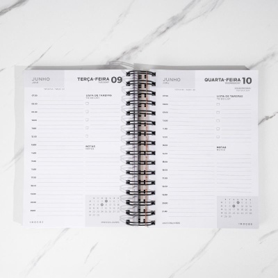 Planner diário aberto em espiral com datas 09 e 10 de junho, em fundo marmoreado branco