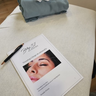 Documento sobre design de sobrancelhas com rosto feminino, caneta e toalha azul dobrada com flor branca num ambiente interior.