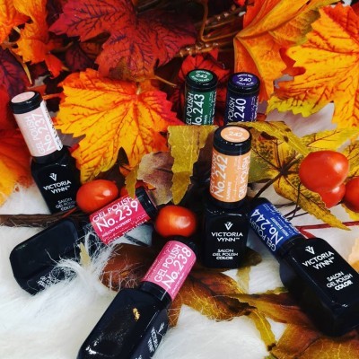 Frascos de verniz gel Victoria Vynn com tampas coloridas numeradas sobre folhas de outono e maçãs vermelhas.
