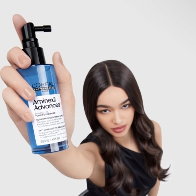 Frasco azul e preto de 100ml do produto L'Oréal Aminexil Advanced com mulher e fundo branco