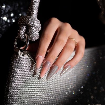 Mão com unhas rosa e prateado segurando bolsa prateada com cristais