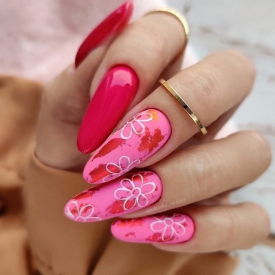 Unhas artificiais com design de manicure em tons de rosa com flores brancas e manchas vermelhas.