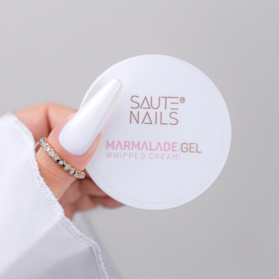 Frasco branco de MARMALADE GEL WHIPPED CREAM SAUTE NAILS segurado por mão com unhas brancas longas e anéis