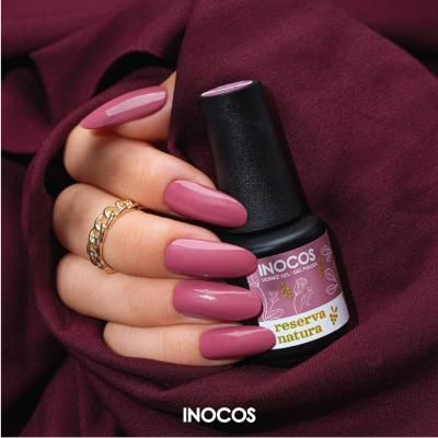 Frasco de verniz gel Inocos Reserva Natura rosa envelhecido com mão segurando com unhas pintadas da mesma cor.