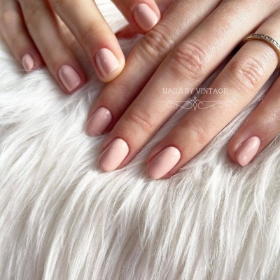 Mãos com unhas pintadas em verniz rosa nude sobre tecido branco felpudo