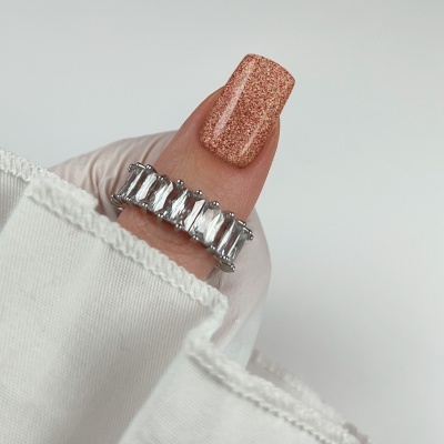 Mão com verniz de unhas cor de bronze brilhante e anel prateado com pedras retangulares