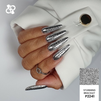 Mão com unhas prateadas brilhantes, anel e gola branca com botão dourado.