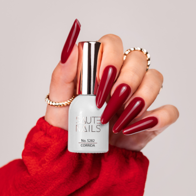 Mão com unhas vermelhas segurando verniz SAUTE NAILS branco