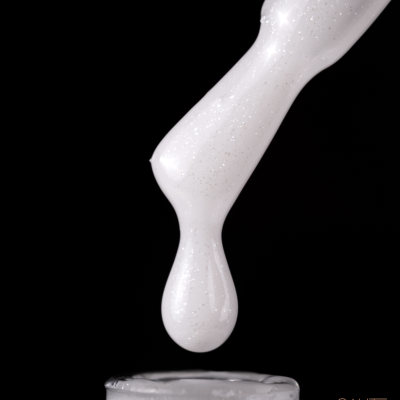 Pincel com gota de verniz branco perolado sobre frasco aberto e fundo preto