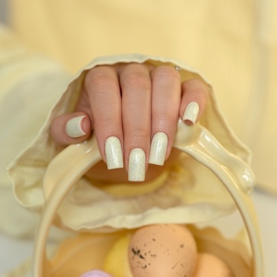 Mão com unhas creme e pontos cinzentos segurando cesta creme com ovos coloridos e manchados.
