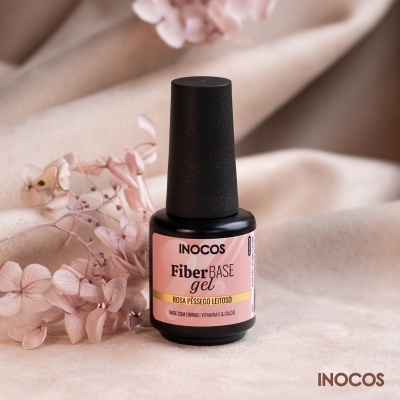 Frasco de verniz em gel INOCOS FiberBASE gel cor rosa pêssego leitoso sobre tecido bege com flores secas cor-de-rosa
