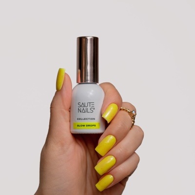 Unhas pintadas em amarelo vibrante segurando um frasco com tampa metálica