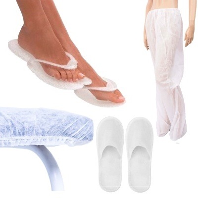 Chinelos descartáveis, calças brancas transparentes, cama de exame com capa protetora e pés com chinelos flip-flop brancos.