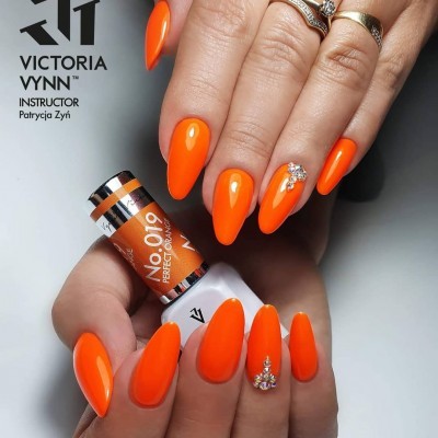 Unhas compridas almendradas com verniz laranja e cristais, segurando frasco de verniz Victoria Vynn laranja.