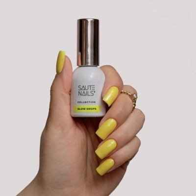 Frasco de verniz para unhas branco com tampa metálica segura por mão com unhas amarelas.