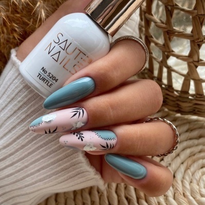 Mão com unhas decoradas segurando frasco de verniz branco Saute Nails