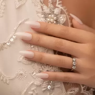 Mão feminina com unhas brancas e anel sobre tecido branco bordado