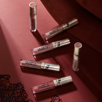 Batons líquidos Varieté em tons rosa e nude com tampas douradas sobre fundo vermelho com padrão rendado