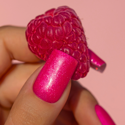 Mão com unhas pintadas de fúcsia segurando uma framboesa rosa com fundo rosa.