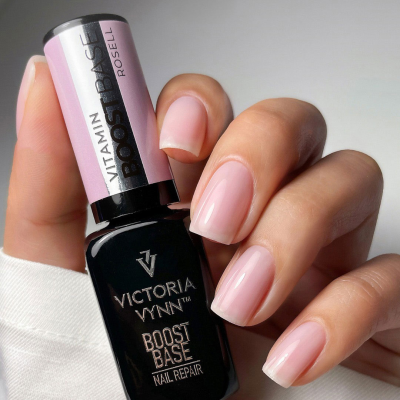 Verniz para unhas Victoria Vynn Boost Base Nail Repair com rótulo rosa e preto segurado por mão feminina com unhas naturais