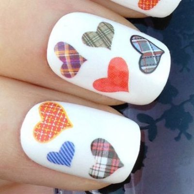 Unhas com verniz branco e corações multicoloridos com padrões xadrez e riscas