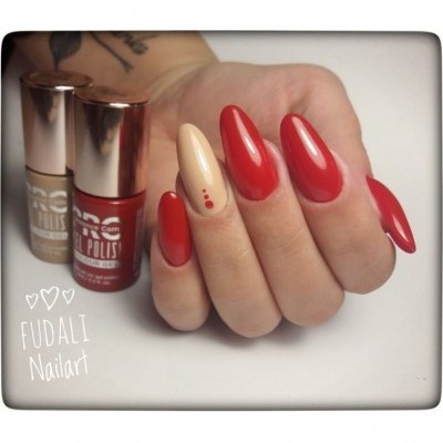 Mano con uñas rojas y diseño beige con puntos rojos junto a botellas de esmalte.