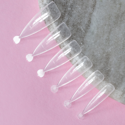 Seis unhas postiças transparentes sobre fundo cor-de-rosa e superfície cinzenta