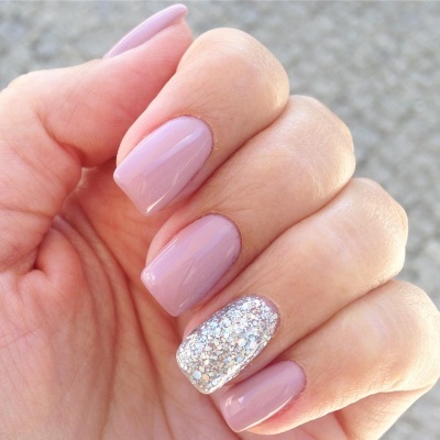 Mão feminina com unhas pintadas em verniz rosa claro e uma unha com glitter prateado