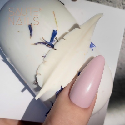 Frasco branco com rótulo 'SAUTE NAILS' e unha pintada de rosa claro fosco