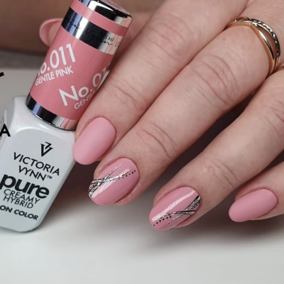 Mãos com unhas pintadas de rosa suave e decoração prateada e preta, com frasco de verniz Victoria Vynn.