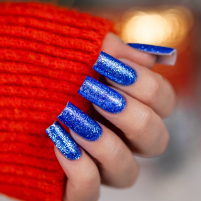 Unhas postiças azuis brilhantes com purpurina em mão com camisola vermelha.