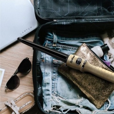 Mala aberta com calções de ganga, nécessaire dourado, aparelho branco e preto, frasco, óculos escuros, sandálias bege, computador portátil branco LAPTOP