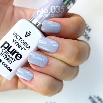 Unhas pintadas de cinza claro segurando frascos de verniz Victoria Vynn