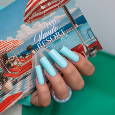Unhas pintadas de azul claro brilhante segurando caixa decorada com guarda-sóis vermelhos e brancos de resort