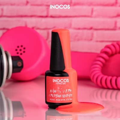 Frasco de verniz gel vermelho INOCOS com tinta derramada e telefone rosa vintage ao fundo