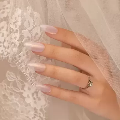 Mão feminina com unhas pintadas de rosa claro e anel prateado segurando tecido de renda e tule branco
