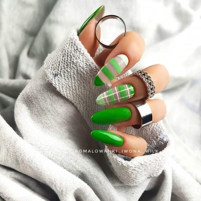 Unhas compridas verdes com design xadrez e anéis em mão feminina segurando tecido cinzento