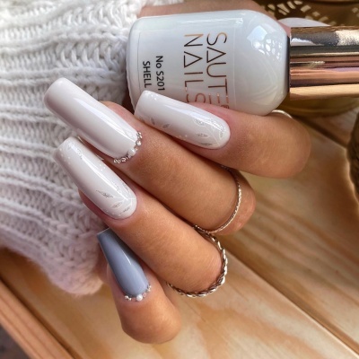 Mão com unhas decoradas em branco e cinzento segurando verniz branco SAUTES NAILS