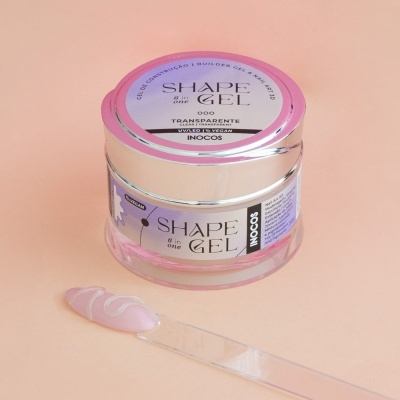 Frasco plástico do gel para unhas SHAPE in GEL com tampa prateada e rótulos rosa, cinza, texto Transparente 000 UV/LED/TRADITION e INOCOS, e espátula com gel à frente.