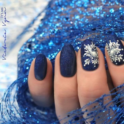 Unhas com verniz azul escuro e detalhes brancos, fundo azul brilhante