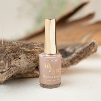 Frasco de verniz de unhas bege com tampa dourada sobre superfície branca e madeira rústica