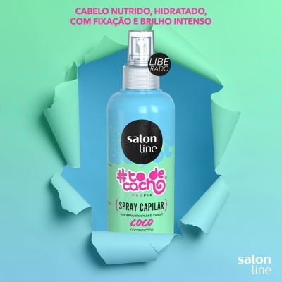 Frasco de spray capilar azul claro com rótulos coloridos e texto em fundo verde e azul com buraco rasgado