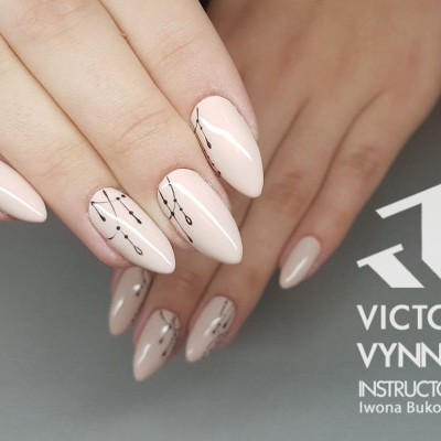 Unhas almendradas com verniz nude e padrão geométrico dourado e preto