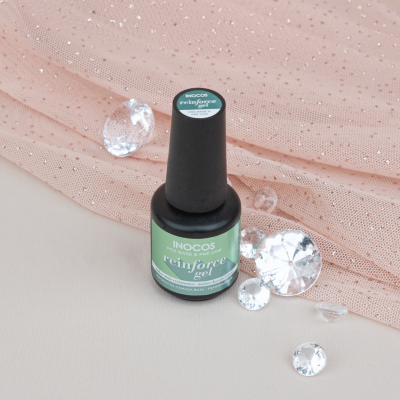 Frasco de verniz de gel verde com tampo preto sobre tecido rosa com pedras decorativas