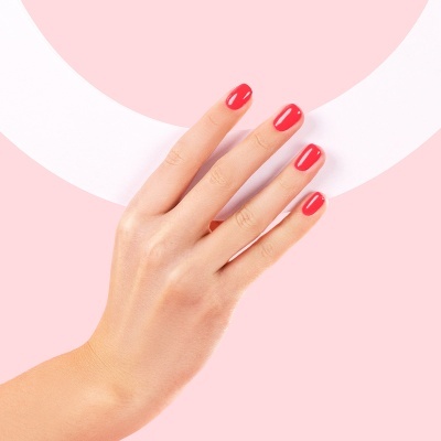 Mão feminina com unhas vermelhas brilhantes em fundo rosa e branco