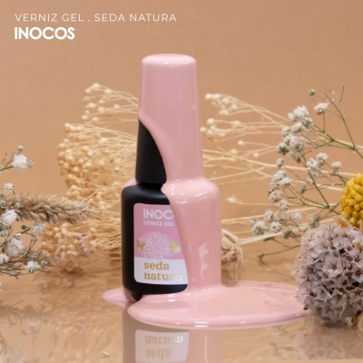 Frasco de verniz gel Inocos com verniz rosa derramado e flores secas ao fundo