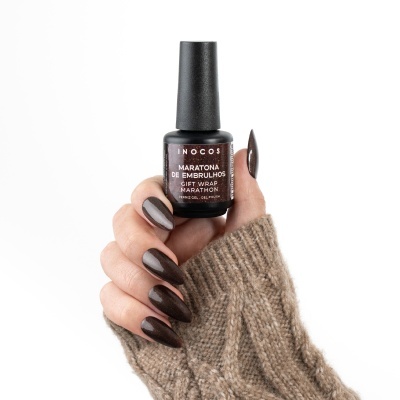 Verniz gel castanho escuro numa mão com unhas pintadas da mesma cor e camisola de malha castanha.
